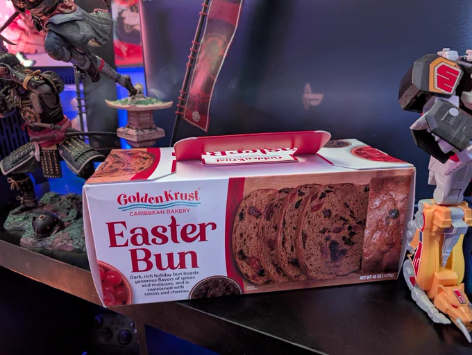 A box of delicious Easter Bun from Golden Krust sits between a Statue from Assassin's Creed: Shadows and a Megazord from Mighty Morphing Power Rangers 