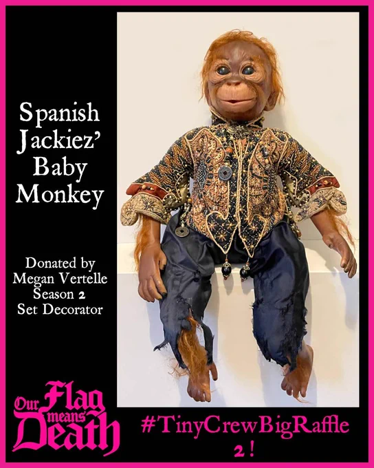 Inticately decorated monkey sits on a stand. White text on a black background states Spanish Jackiez' Baby Monkey - Donated by Megan Vertelle Season 2 Set Decorator. In Pink text it says Our Flag Means Death #TinyCrewBigRaffle2
