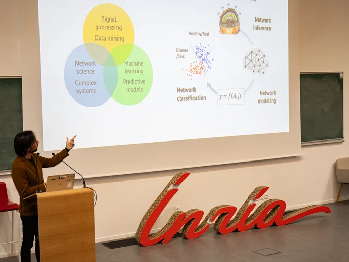 Photo de Fabrizio de Vico Fallani sur la scène de l’amphithéâtre du Centre Inria de Paris, présentant les axes de recherche de son équipe NERV