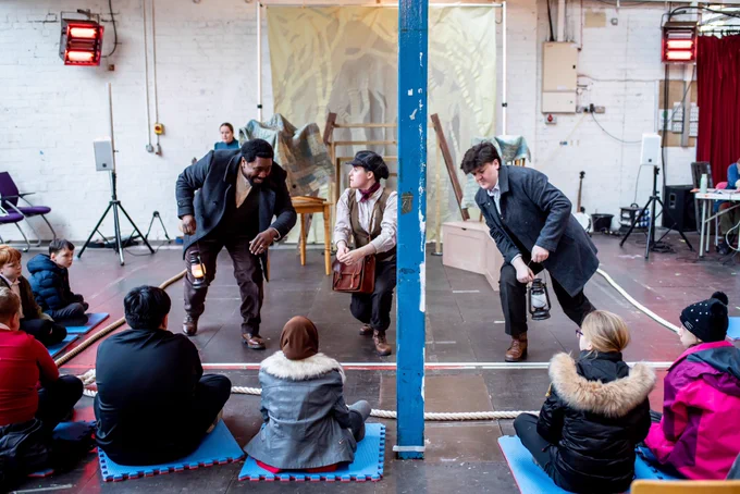 A company of four actors performing in front of a small group of primary school children in a warehouse.