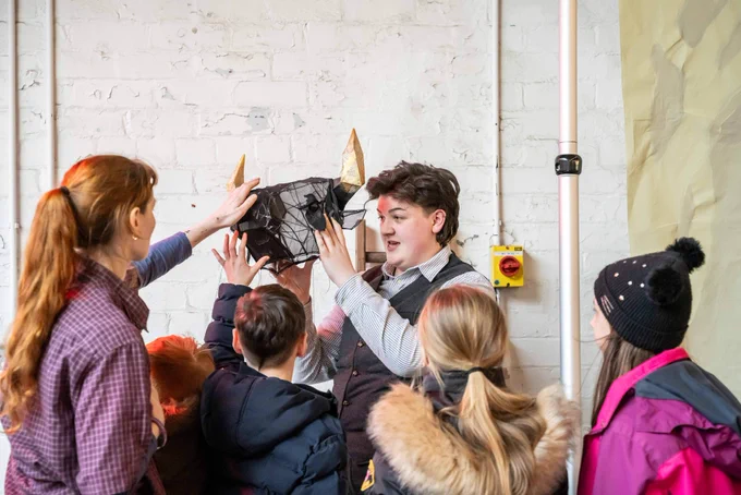 A group of children reaching out to touch the Minotaur prop head made of wire, gauze and gold book pages.