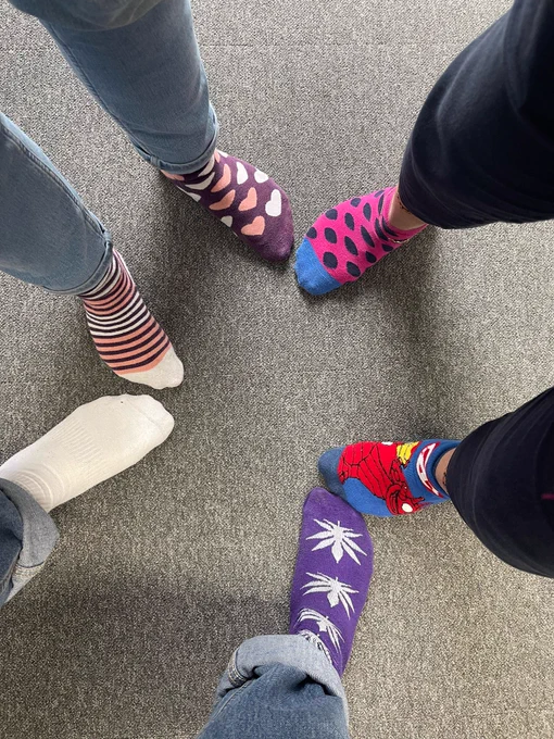 Three pairs of feet all wearing different brightly coloured odd socks. 