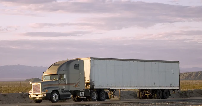 A semi-truck with a large trailer parked in a vast, open desert landscape during twilight.