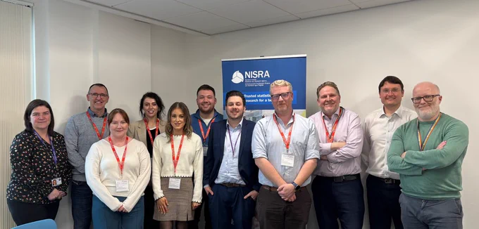 Photograph of Perm Sec @dptfinance Neil Gibson and NISRA CEO Philip Wales congratulating the NI PfG Wellbeing Framework Development team for their recent success in the Analysis in Government (AiG) Awards.