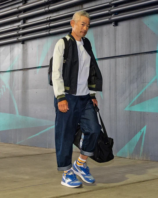 Ichiro Suzuki walking into T-Mobile Park. He's wearing a black and white jacket, white shirt, dark blue jeans, and blue and white shoes. He's a black gym bag.