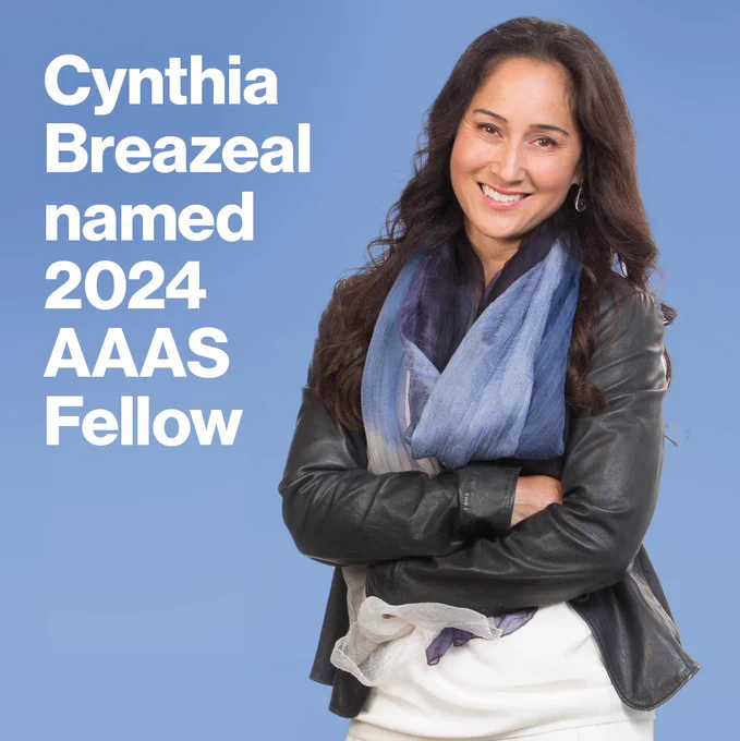 Portrait of Professor Cynthia Breazeal. Her arms are crossed and she is smiling, wearing a black leather jacket and a blue scarf. Beside her is white text that reads "Cynthia Breazeal named 2024 AAAS Fellow."