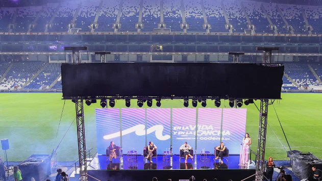 Vista panorámica del escenario principal del evento "M En la Vida y en la Cancha" en el estadio de fútbol BBVA, con asistentes sentados observando una charla sobre el campo.