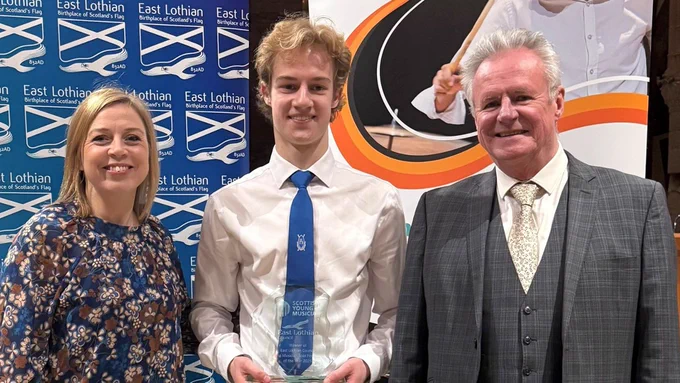 Young Musician of the Year Thomas Bull, holding a glass trophy, stands between adjudicators Katrina Marzella-Wheeler and Michael McGeary in St Mary's Church, Haddington.