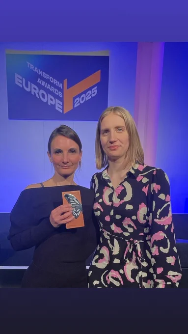 two people standing together with the first holding an award decorated with half a butterfly wing