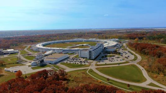Aerial photo of the Advanced Photon Source in autumn, surrounded by trees with red and brown leaves. 