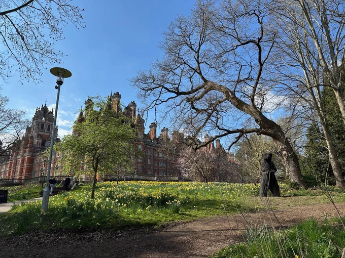 A photograph of Founders building with the statue of Colossus in the foreground and the bank leading up to the terrace covered by daffodils 