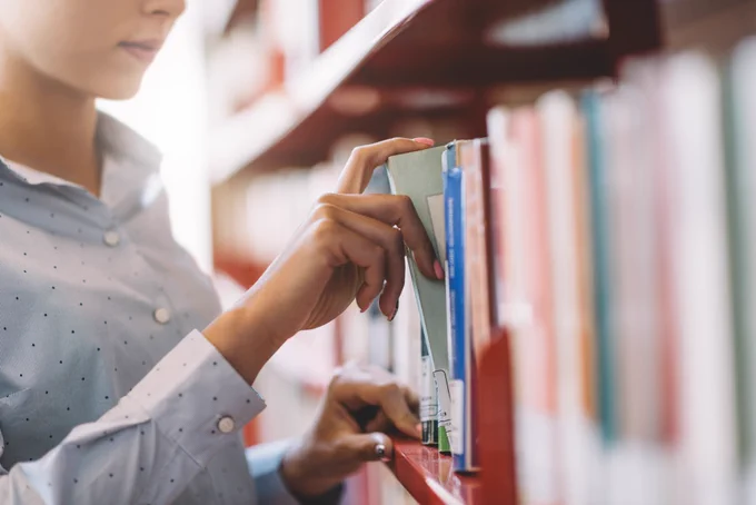 Person pulling a book off a library bookshelf.