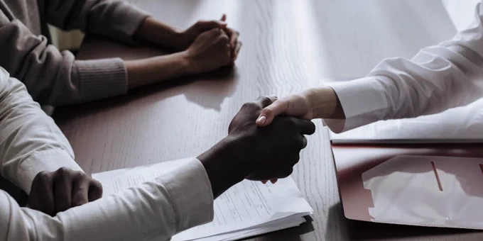 Business agreement with a handshake over contract documents at a meeting table.