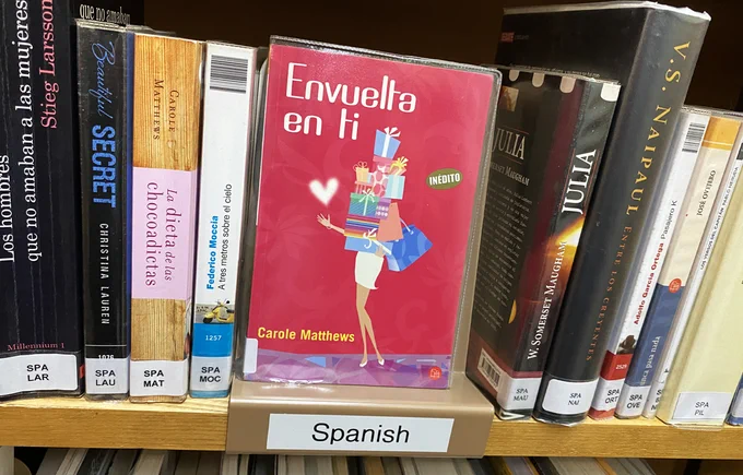 A row of Spanish books in a library with a focus on "Envuella en ti" by Carole Matthews.