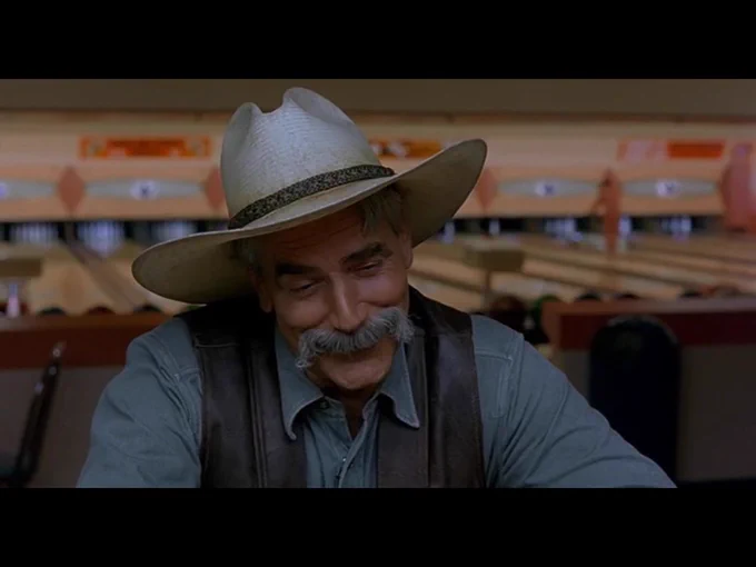 The Stranger, now in close-up, chuckles to himself as he turns back to the bar.