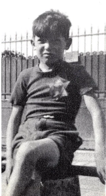 Black and white photo of a young boy sitting casually on a railing, wearing a t-shirt with a star of David.