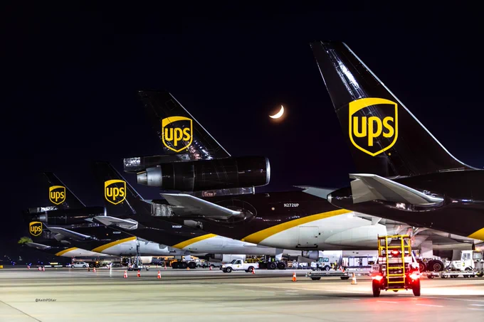 Five UPS aircraft parked in a neat row on the tarmac at Louisville airport, illuminated by the night lights.