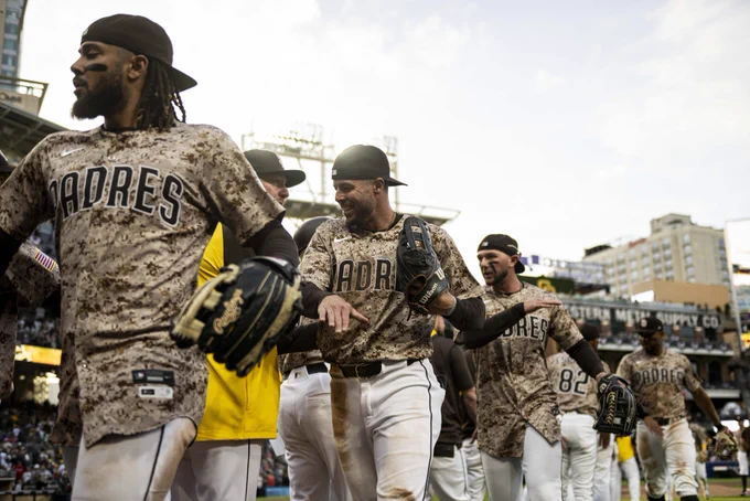 Photo of Fernando Tatis Jr., Brandon Lockridge, and Jackson Merrill walking through the Padres high five line after sweeping the Braves. They are wearing the Padres tan camo uniform that is worn each SD Military Sunday.