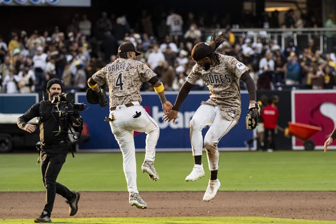 Photo of Fernando Tatis Jr. and Luis Arraez jumping up and high-fiving each other after today’s sweep of the Braves. They are both wearing the Padres tan camo uniform that is worn each SD Military Sunday.