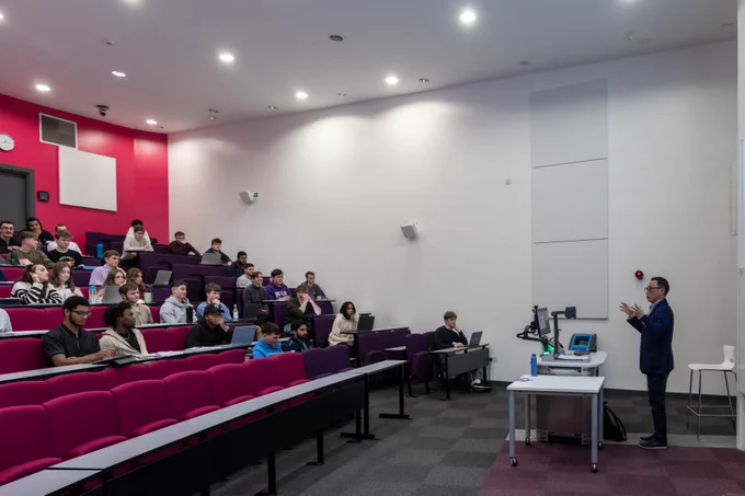 A person giving a lecture on the right, people sitting in tiered seating to the left