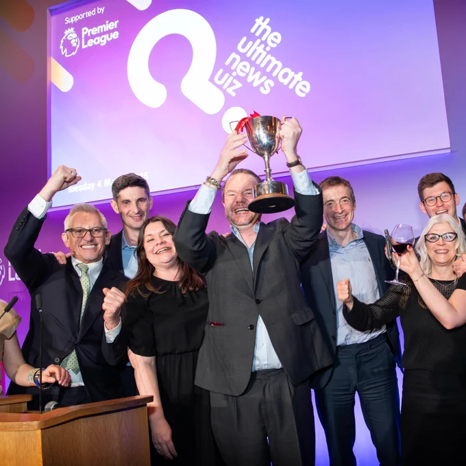 A group of individuals celebrating with a trophy at "The Ultimate News Quiz" event supported by the Premier League.