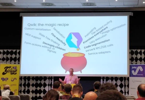Wout standing in front of a slide with a cauldron and a Qwik logo whole holding out his hands