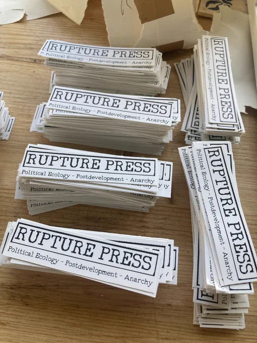 smaller rectangular stickers with the text RUPTURE PRESS, and the words political ecology- postdevelopment- anarchy