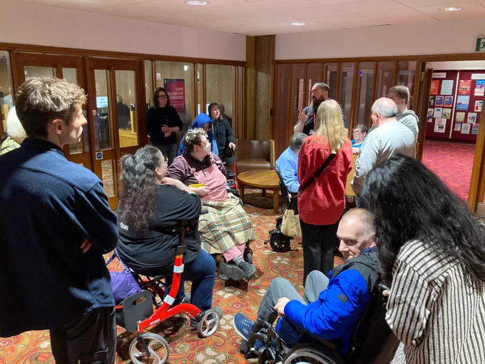 A group of GDA members in a common space style room, listening to a tour guide.