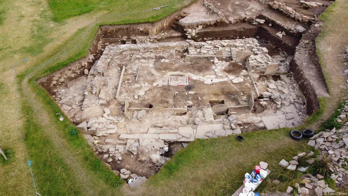 Aerial photo of the excavation of a prehistoric stone building with low walls and hearths visible