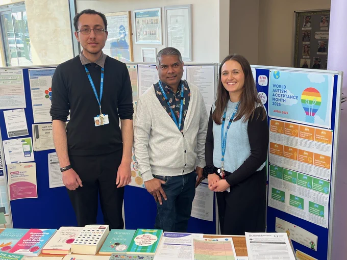 Three people stood at stall in reception for World Autism Acceptance Month 