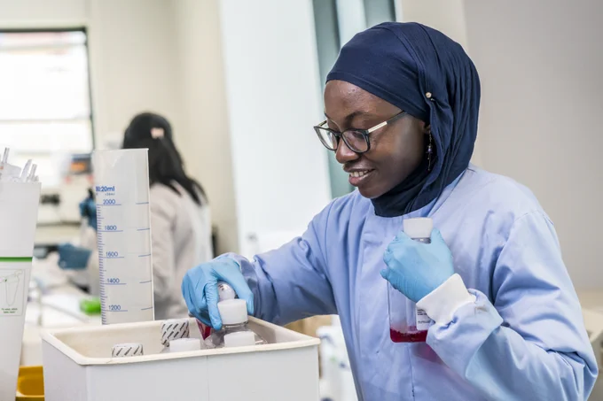 An image of a student in a laboratory, wearing a blue lab coat and a headscarf.