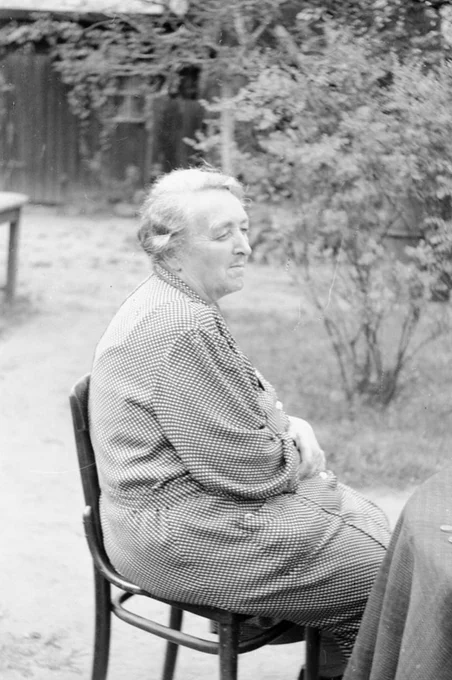 An older woman sitting in a chair in a garden.