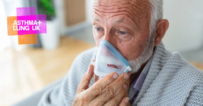 A man is holding an oxygen mask on his face as he uses his ventilator at home.
