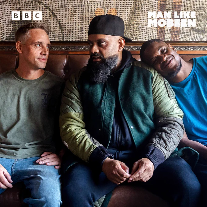 Harper, Mobeen and Nate sit closely on a sofa. Mobeen looks serious while Harper smiles at him, and Nate rests his head on Mobeen’s shoulder.