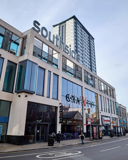 Exterior view of the Southside building in an urban area, featuring signage for Gravity and other businesses on the ground floor, with a tall residential tower visible in the background.