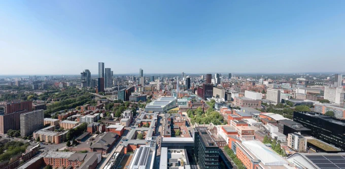 Aerial view of Manchester city centre showcasing modern high-rises and traditional architecture amidst expansive green spaces.