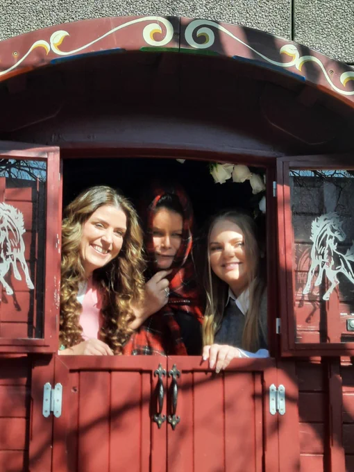 Three people look out from inside a traditional Traveller wagon