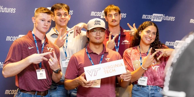 Photo of team doing the VT hand symbol and one holding a Virginia Tech sign. 