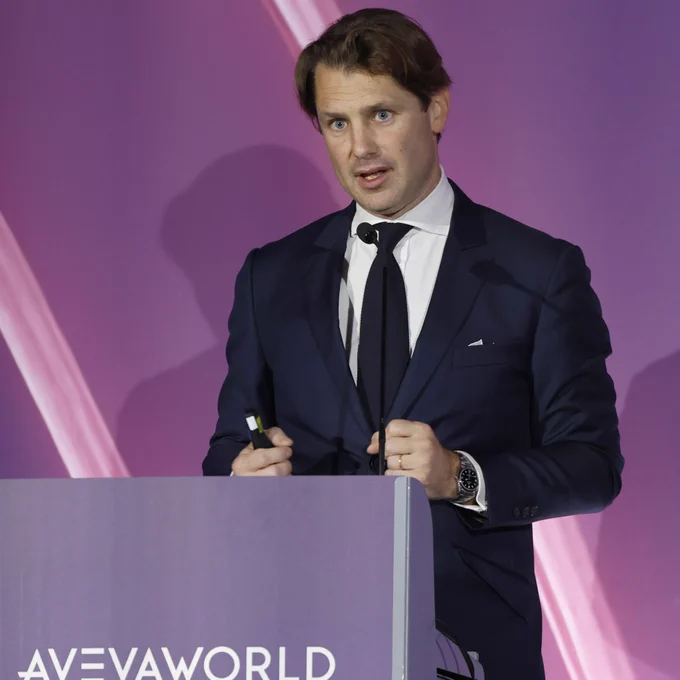 man behind podium speaking in front a purple backdrop