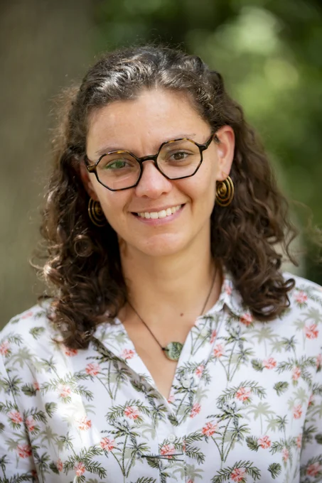 portrait of a person with curly dark hair and glasses wearing a floral button down shirt