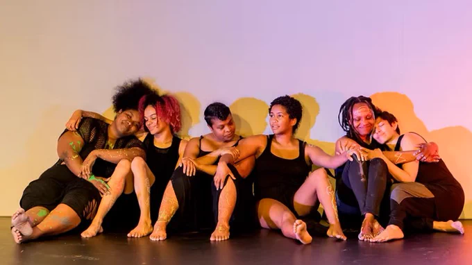 A group of Black women sitting on the ground and hugging