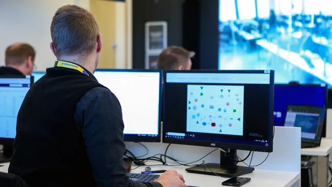 Henkilöitä istumassa tietokoneruutujen äärellä kuvattuna takaapäin.