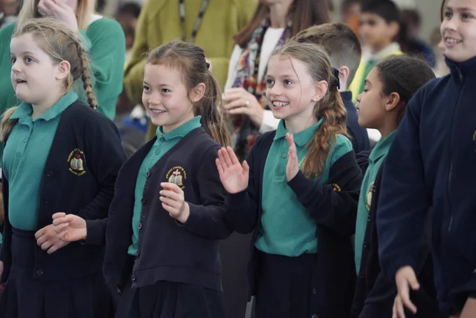 Disgyblion ysgol mewn gwisg ysgol, canu a chlapio.