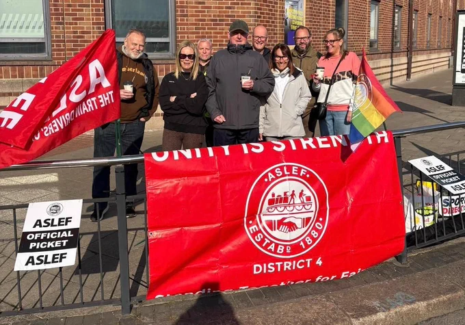 People standing on a picket line with ASLEF banners and flags