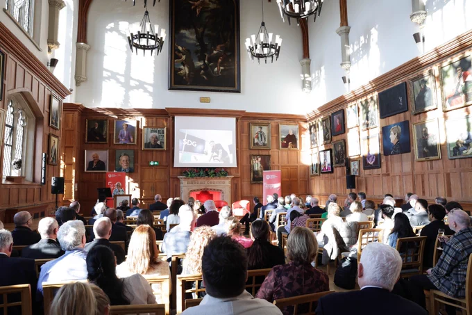 Image shows the crowd at the event taken from the back of the Great Hall. Wendy Austin MBE is speaking on the stage.