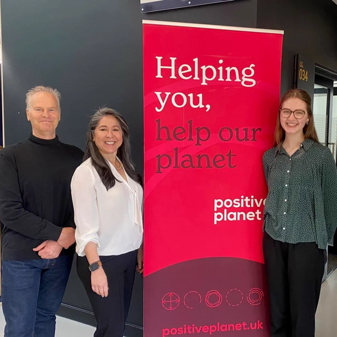 Representatives from Keele University and Positive Planet smiling while standing in front of a red pull-up banner