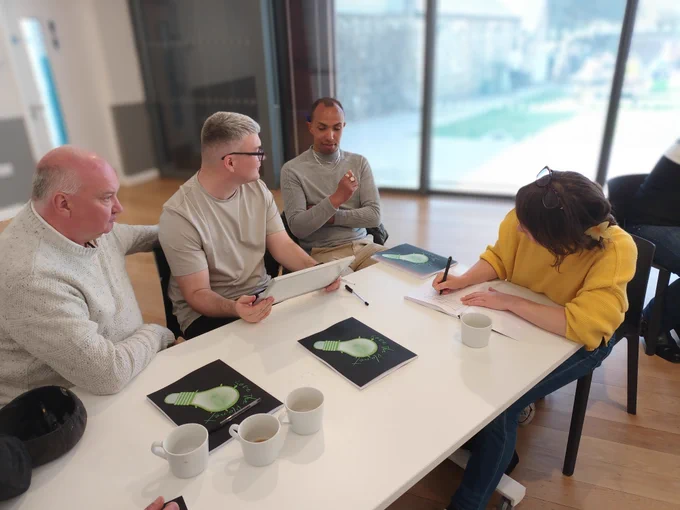 4 individuals sitting around a table talking, 1 person taking notes