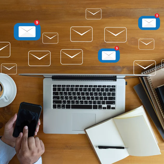 Person at desk with smart phone, laptop, note pad and pen.  Mailing envelope icons.
