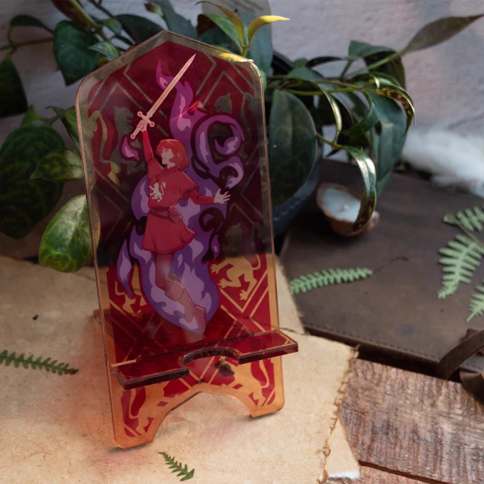 The Alanna Acrylic Phone Standee placed on top of some tattered papers with various greenery surrounding it.