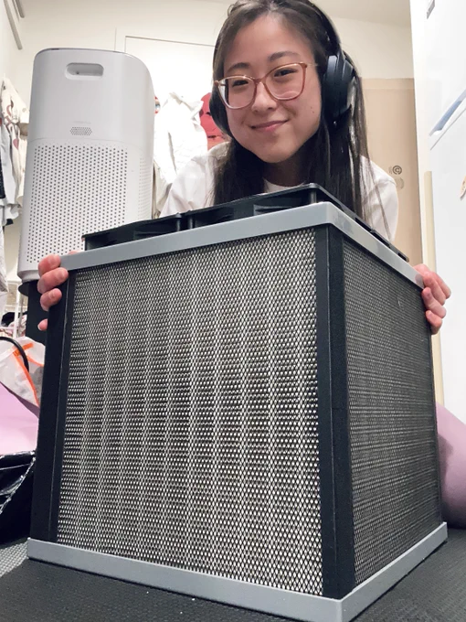 Author of tweet smiling and hovering behind the AirFanta 3Pro air purifier, which is in the center of the photo on the floor, with two of its white colored filter panels with wire mesh over it, and fans on the top. 